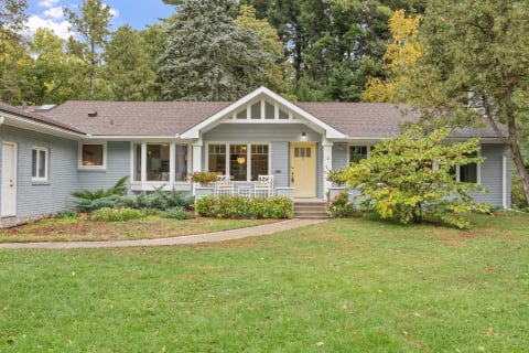 Single-story house with gray exterior, yellow door, and green front yard.
