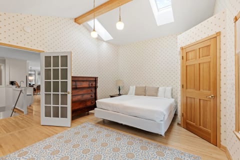 Cozy bedroom with a white bed, wooden dresser, and patterned wallpaper.