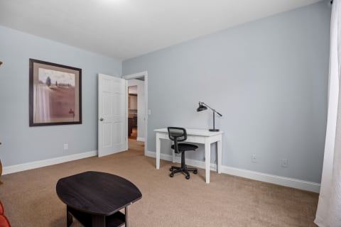 A room featuring light blue walls, a white desk, and a framed artwork.