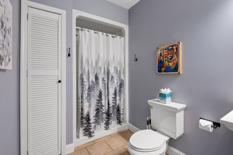 Modern bathroom with lavender walls, a shower curtain with evergreen trees, and artistic decor.