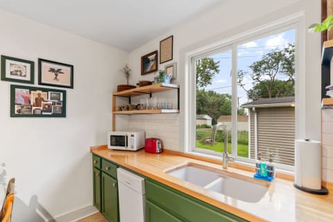 A modern kitchen corner featuring green cabinets, a wooden countertop, and framed artworks.