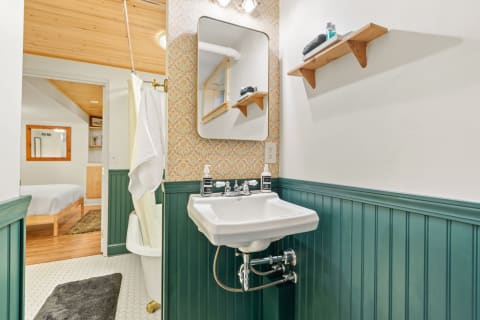 A cozy bathroom with green wainscoting, patterned wallpaper, and a white sink.