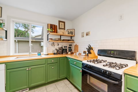 Bright kitchen featuring green cabinets, wooden countertops, and a view through the window.