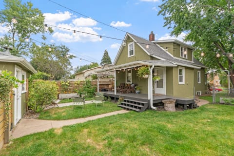 Outdoor view of a green house with a deck and garden, surrounded by trees and decorative lights.