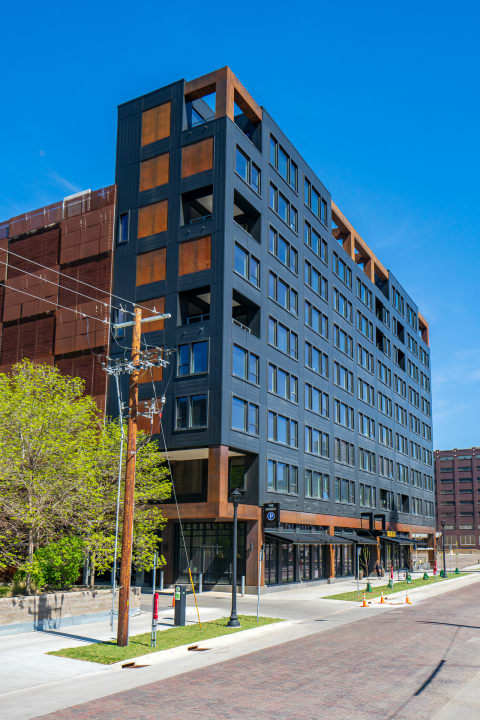 Contemporary multi-story building with gray and copper accents featuring large windows and retail spaces.