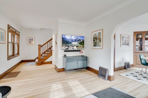 Cozy living room with a large TV, gray media console, and natural wood staircase.