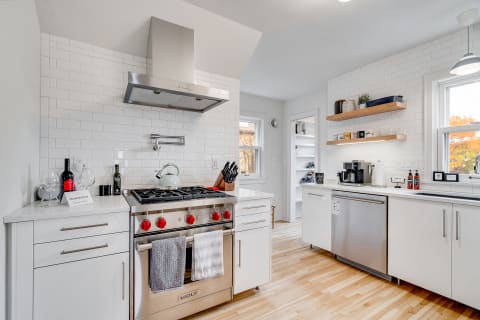 Modern kitchen with white cabinets, stainless steel appliances, and wooden shelves.