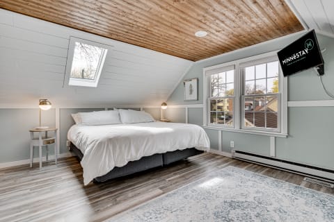 A stylish bedroom with a sloped white wooden ceiling, a large bed, and natural light from a skylight.