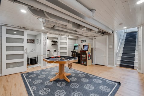 Interior view of a modern basement with a pool table, arcade games, and laundry area.