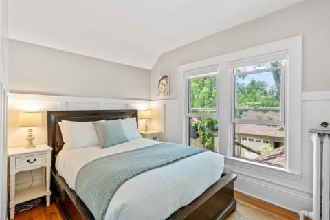 A bright and inviting bedroom with a dark bed frame, blue accents, and large windows overlooking greenery.
