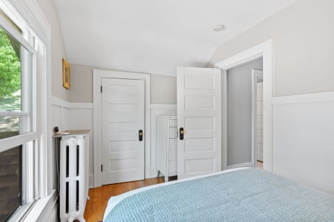 Interior view of a cozy bedroom featuring a sloped ceiling, vintage radiator, and light blue blanket on the bed.