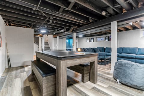 Modern basement interior featuring a game table, seating area, and decorative elements.