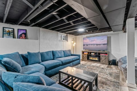 A spacious basement living room featuring a blue sectional couch, coffee table, and large TV on the wall.