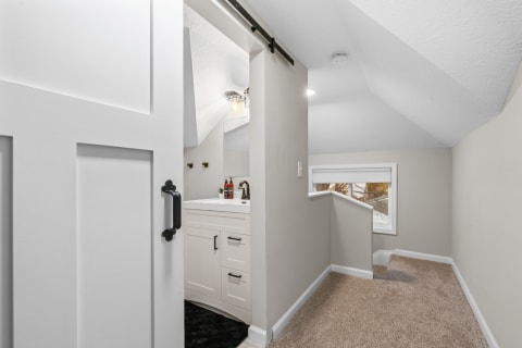 Cozy loft bathroom featuring a white vanity and soft beige walls with a sliding barn door.