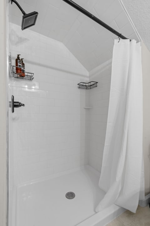 A modern shower featuring white subway tiles, a black showerhead, and a white curtain.