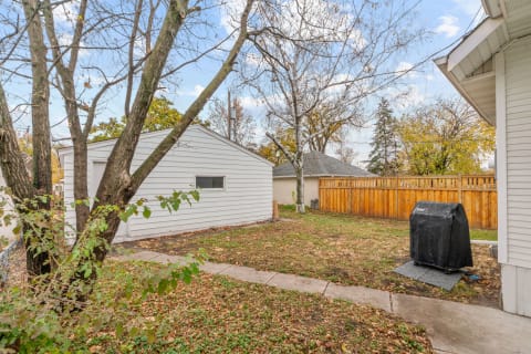 Backyard with a white shed, a large tree with bare branches, a concrete path, and a covered grill.