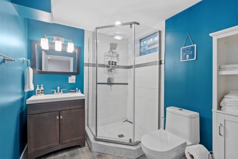 Modern bathroom featuring turquoise walls, a dark wooden vanity, and a frameless shower.