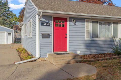 A light blue house featuring a red front door and a garage in the background.