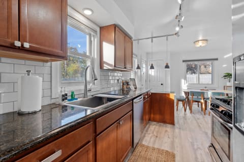 A contemporary kitchen with dark granite countertops, wooden cabinets, and a dining area with blue chairs.