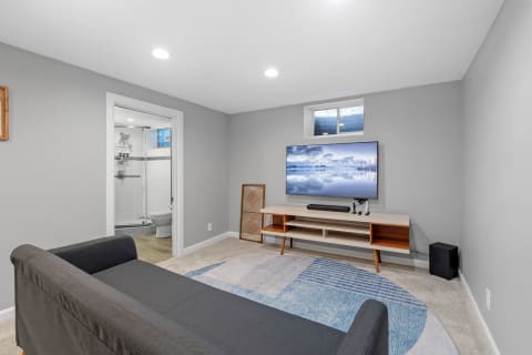 A stylish living room with a flat-screen TV, gray sofa, and an open bathroom in the background.