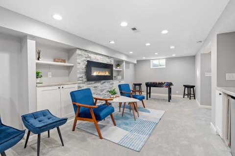 Modern basement living area with blue seating, a stone fireplace, and a foosball table.