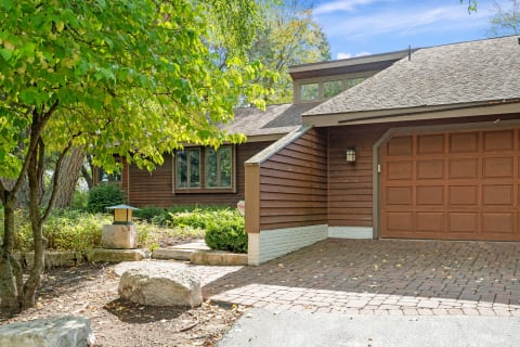 A modern home with wood siding, large windows, and a brick pathway surrounded by greenery.