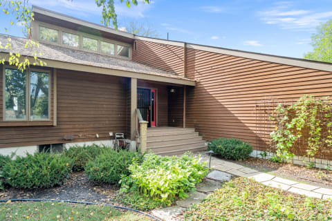 Exterior view of a modern house featuring brown wooden siding and a red front door.