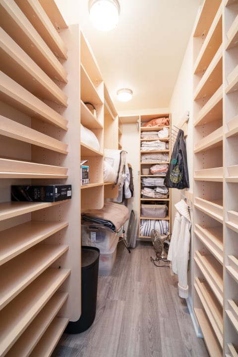Narrow closet featuring wooden shelves filled with linens and clothing.