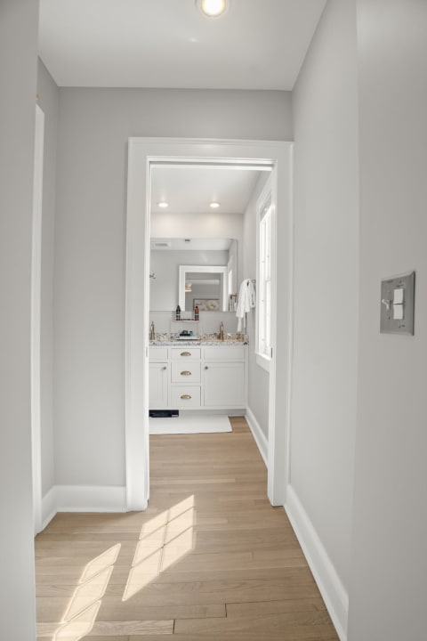 Hallway leading to a bathroom with white cabinetry and sunlight filtering through.