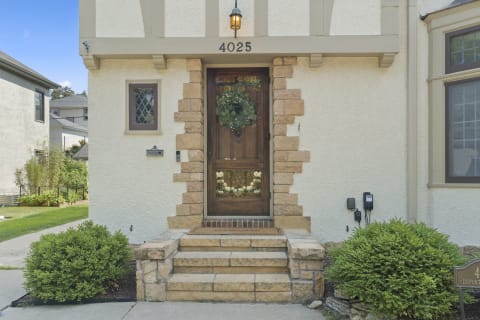 Charming house entrance with wooden door, stone steps, and green shrub.