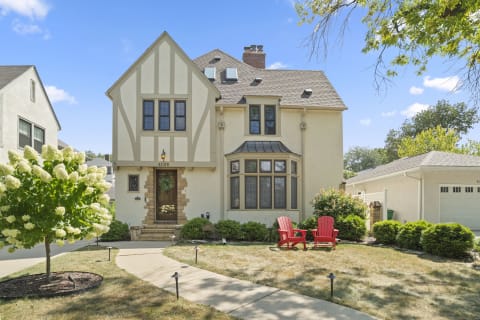 Tudor-style house with a welcoming front lawn, red chairs, and blooming hydrangea tree.