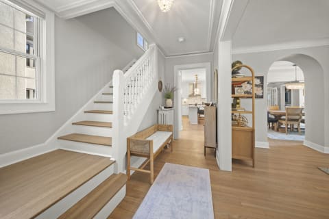 An entryway featuring gray walls, hardwood floors, a staircase, and cozy furnishings.