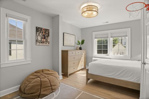 Bright bedroom with basketball-themed decor, featuring a plush ottoman and natural light.