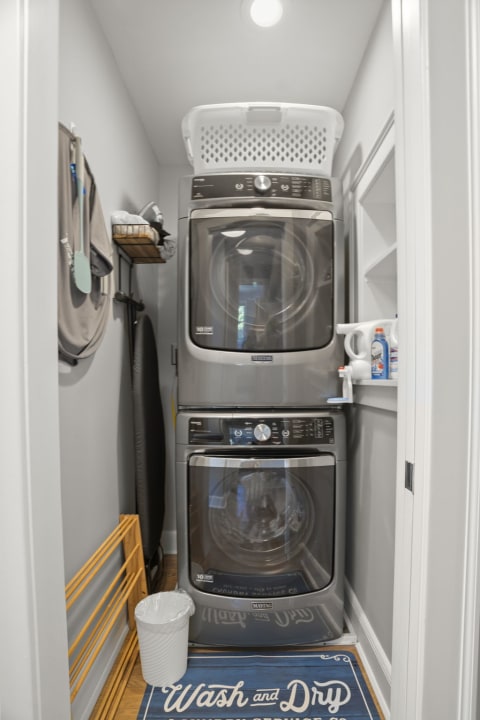 Modern laundry area with stacked washer and dryer, white shelving, and a vibrant blue rug.