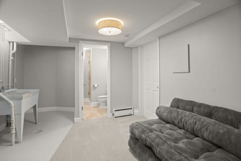 Cozy lower-level retreat with a gray sofa, utility sink, and doorway to a bathroom.