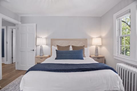 A tranquil bedroom with a bed dressed in white linens, soft throw pillows, and warm light streaming through a window.