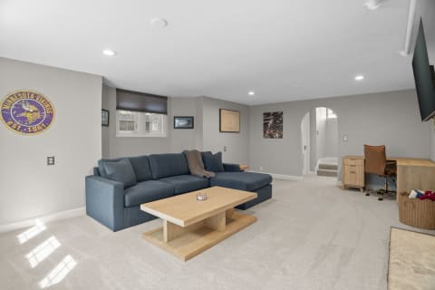 Cozy lower-level living space featuring a large sectional sofa, wooden coffee table, and natural light filtering through blinds.