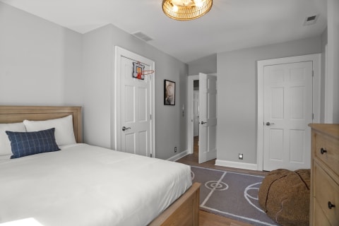 A cozy bedroom with a basketball hoop on the wall, featuring a plush bed, a basketball-themed rug, and warm lighting.
