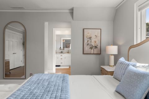 Serene bedroom with blue bedding, mirror, and a glimpse of an en suite bathroom.