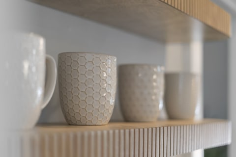 Ceramic mugs with varying textures displayed on a wooden shelf.