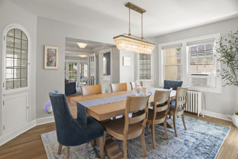 Light-filled dining room featuring a large wooden table, blue upholstered chairs, and a sparkling chandelier.