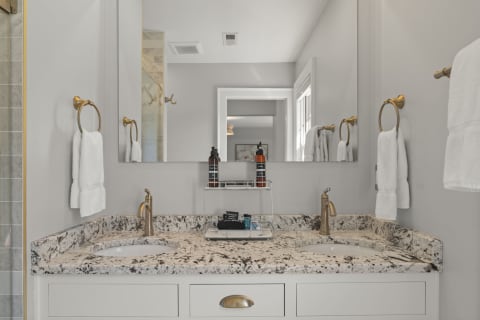 A luxurious double vanity in a bathroom with granite countertops, gold fixtures, and white towels.