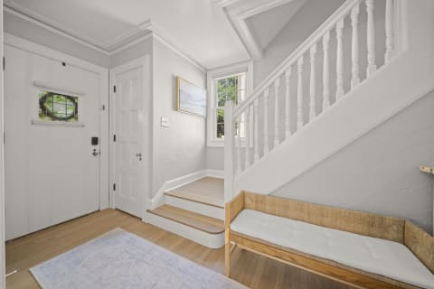 Welcoming entryway with a wooden bench, light gray walls, and a staircase leading upstairs.