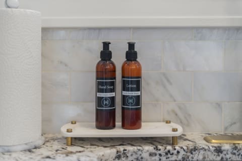 Elegant hand soap and lotion displayed on a marble tray with gold accents against a marble tiled wall.