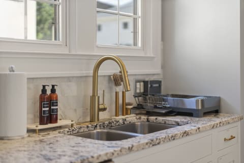Modern kitchen sink featuring a brass faucet, granite countertops, and natural light from a large window.