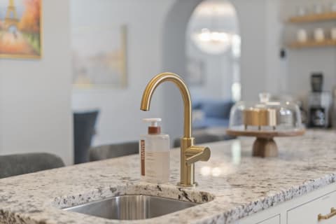 A stylish kitchen with a brass faucet, granite countertop, and blurred living area in the background.