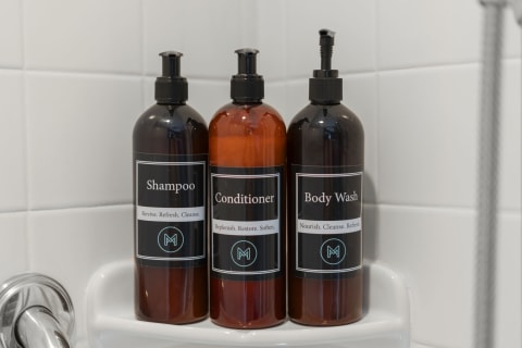 Three bottles of shampoo, conditioner, and body wash arranged on a shelf in a shower, displaying their labels.