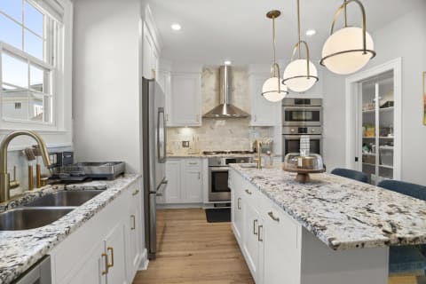 A modern kitchen featuring granite countertops, stainless steel appliances, and a spacious island with pendant lighting.