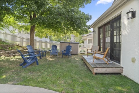 A backyard retreat with blue Adirondack chairs, a low wooden deck, and shade from a large tree.