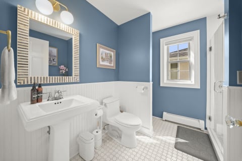 A stylish bathroom with blue walls, white fixtures, and natural light filtering in through a window.
